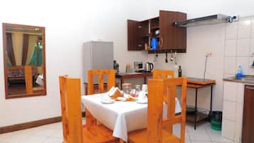 Cocina compacta con una mesa de comedor dispuesta para cuatro personas, sillas de madera, horno empotrado y una pequeña encimera con un hervidor y otros utensilios de cocina.