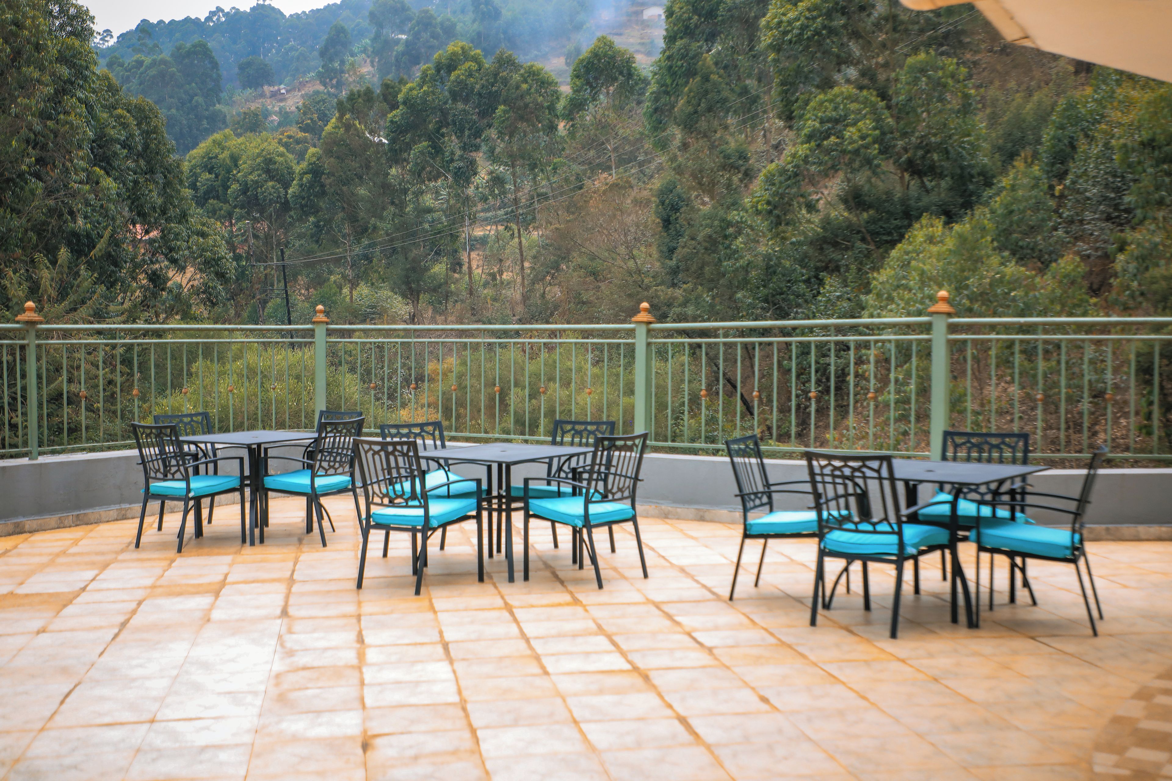 An outdoor patio with tables and chairs, surrounded by a green fence and trees.