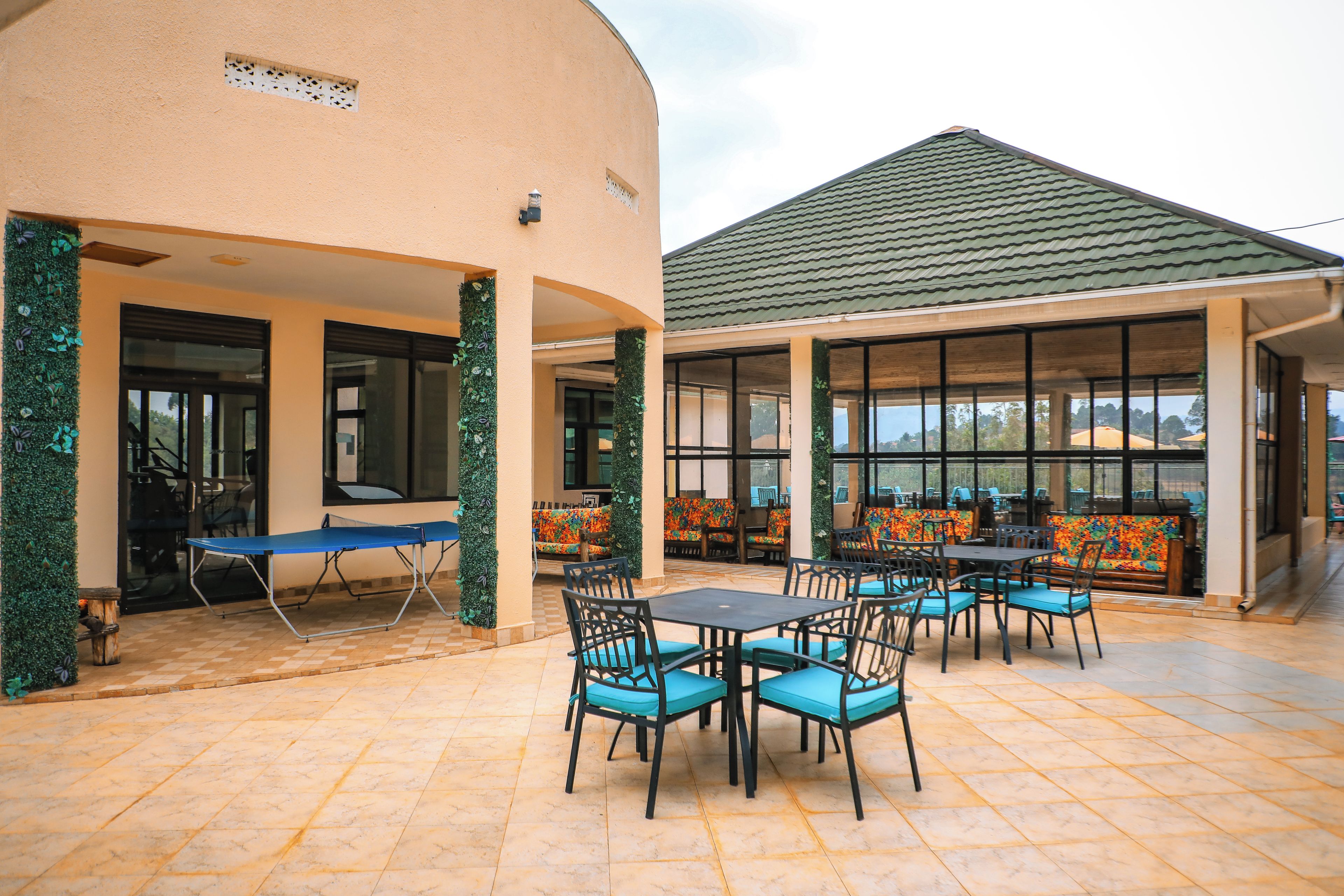Un espacio al aire libre con mesas y sillas, una mesa de ping pong y una zona de estar cubierta con cojines de colores.