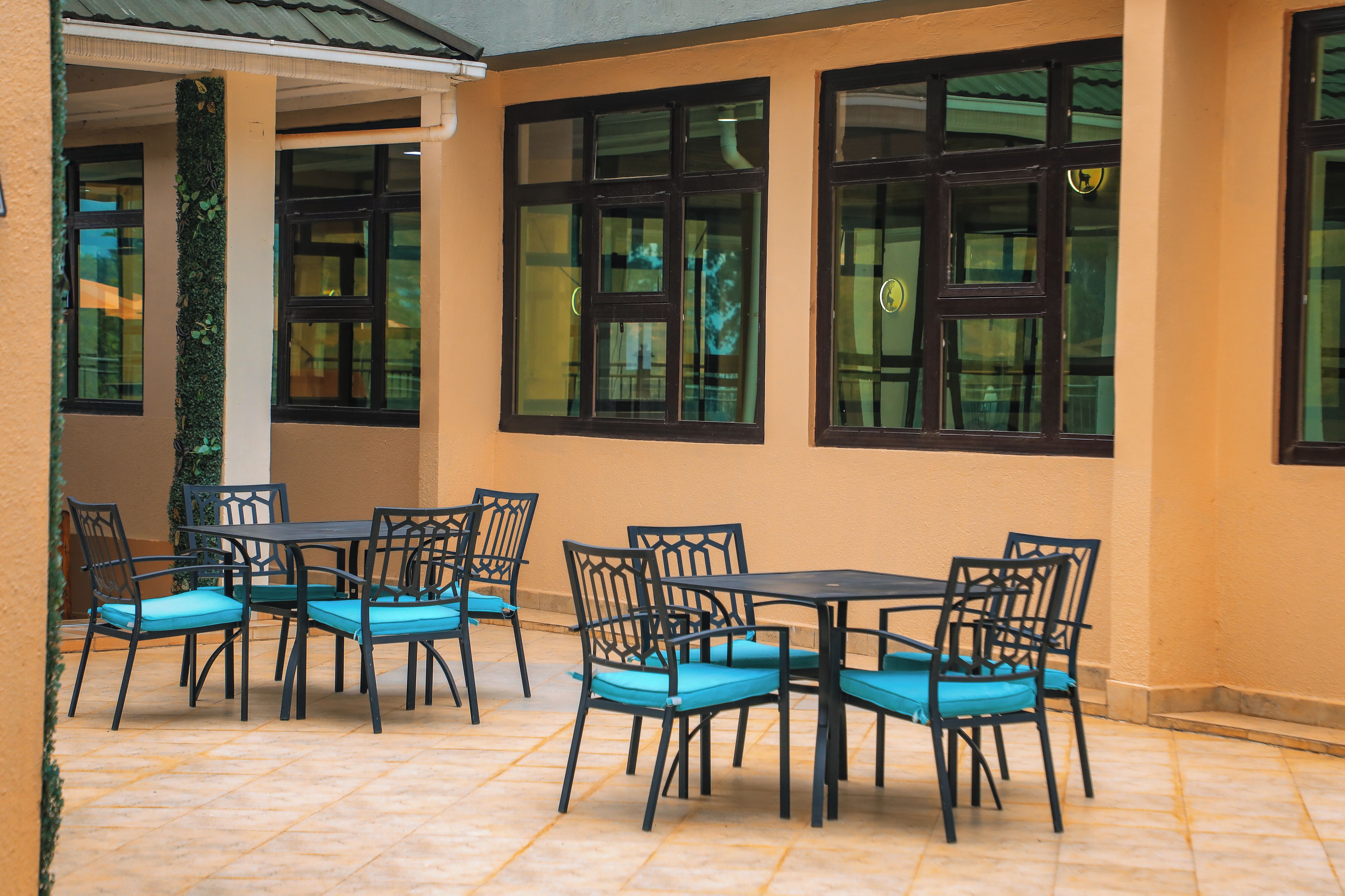 An outdoor patio area with multiple tables and chairs, a tiled floor, and large windows with dark frames.
