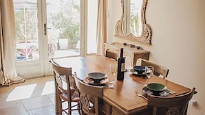 Zona pranzo con tavolo in legno, sedie, una bottiglia di vino e uno specchio a parete.