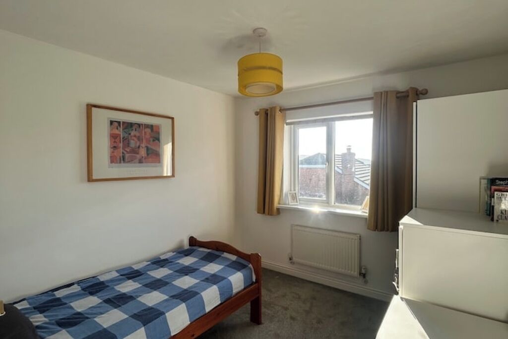 Une chambre avec un lit simple, une fenêtre avec des rideaux, un radiateur et un luminaire au plafond.