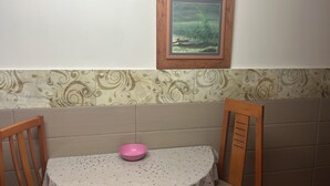 Un comedor con una mesa redonda, un bol rosa y dos sillas de madera. Un cuadro enmarcado cuelga de la pared sobre la mesa.