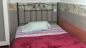 Una cama con una manta roja, cabecera de metal y pared con diseño.