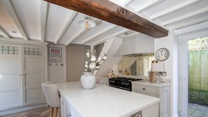 A kitchen with white cabinetry, a marble island, wooden stools, a gas stove, and a clock on the wall. - Rainbow Cottage (Ormskirk)