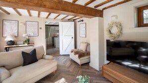A living room with a sofa, a television, wooden beams on the ceiling, and framed artwork on the walls. - Rainbow Cottage (Ormskirk)