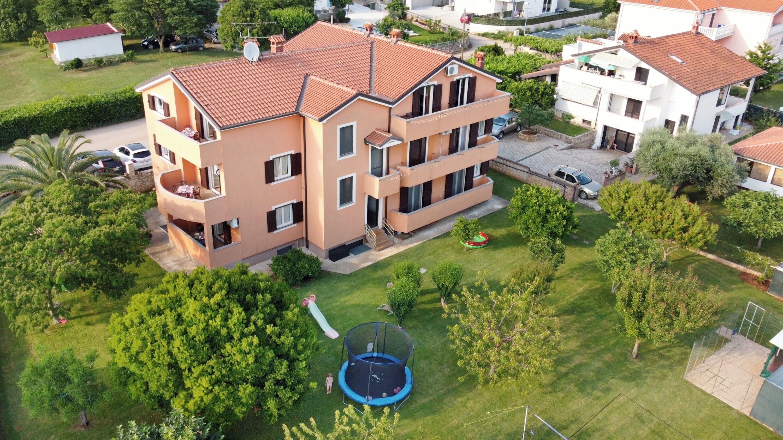 Ein mehrgeschossiges Wohngebäude mit rotem Ziegeldach, einem Balkon und einem kleinen Trampolin im Hof.