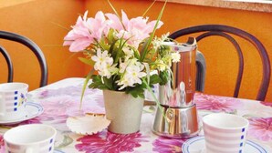 Ett bord dukat för två personer, med en blommig duk, en vas med blommor och en silverkanna.