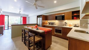 A modern kitchen with wooden cabinets, a central island, and a dining area with chairs. - Short Walk to Beach & Town · Top Level · Solana (Huatulco)