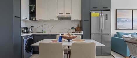 A modern kitchen with a built-in washer and dryer, a dining area with a table and chairs, and a grey refrigerator.