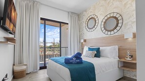 Une chambre d’hôtel moderne équipée d’un lit, d’une télévision, d’un balcon et de miroirs décoratifs sur les murs.