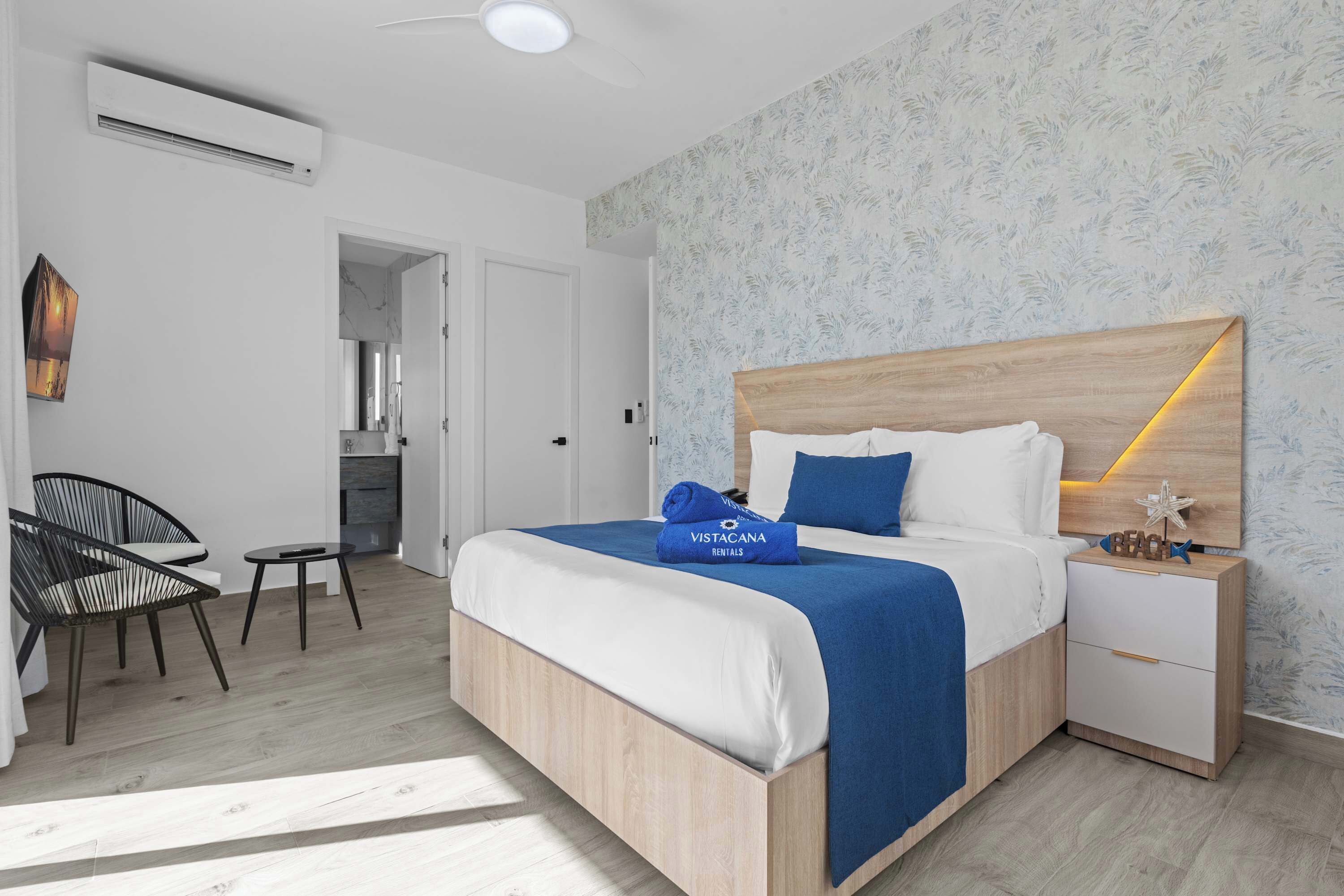 Une chambre d’hôtel moderne avec un lit en bois, une table de chevet, une chaise et une petite table.
