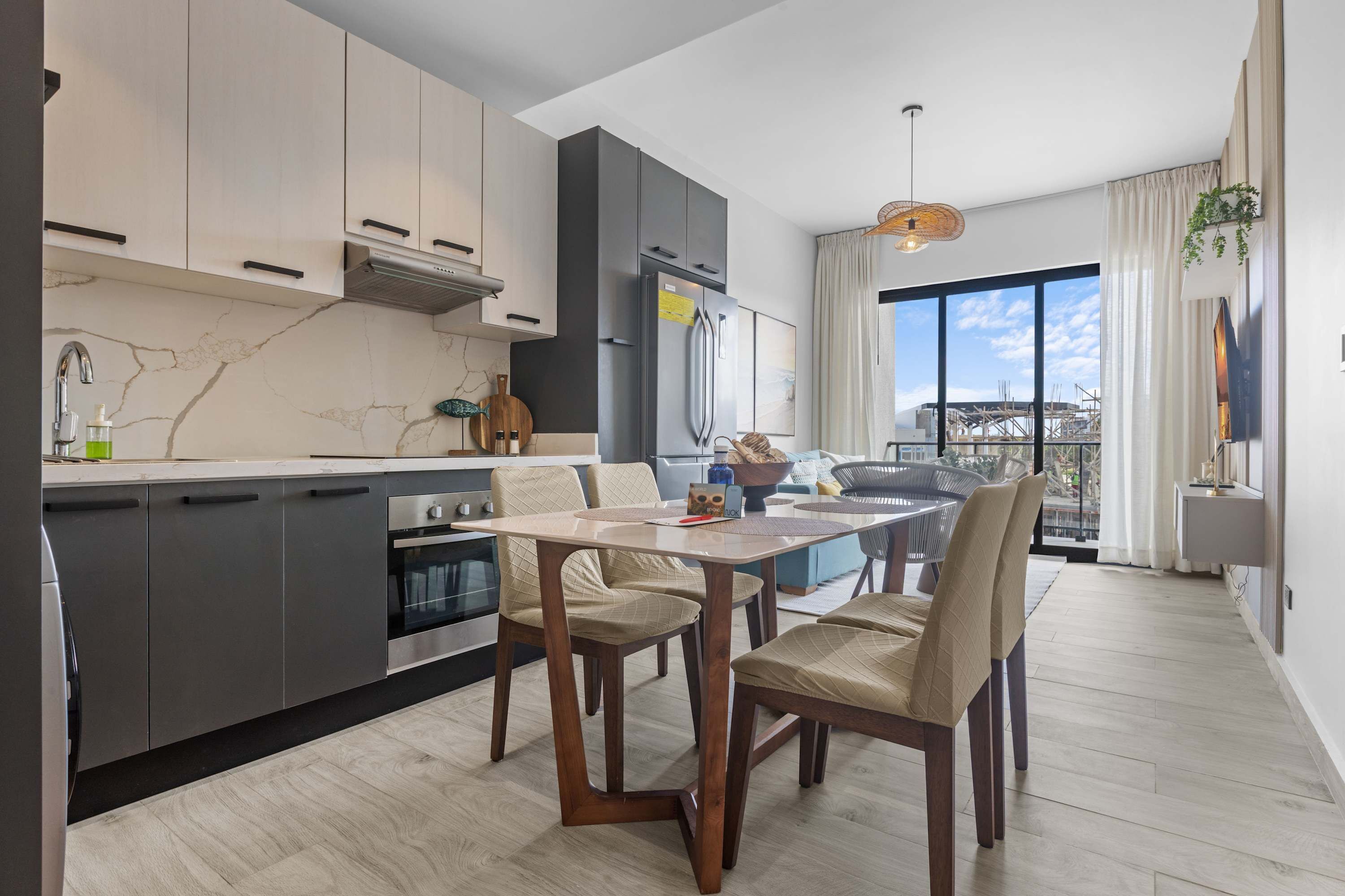 A modern kitchen with dark cabinets, a marble backsplash, and a dining area with a table and chairs.