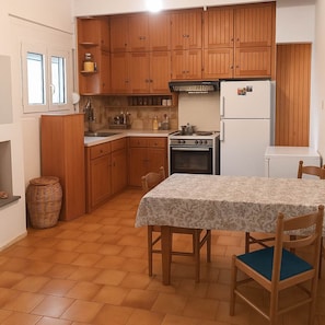 A compact kitchen with wooden cabinets, a stove, a refrigerator, and a dining table with chairs.