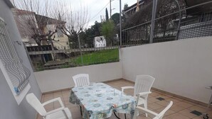 Un patio con una mesa y cuatro sillas, rodeado de un suelo de baldosas y una pared blanca.