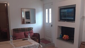 Un área de comedor con una mesa preparada para dos, un sofá con cojines, un televisor sobre la chimenea y un espejo en la pared.