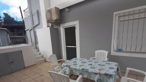 Un patio con mesa y sillas, una zona de estar cubierta y vistas a un edificio con una escalera.