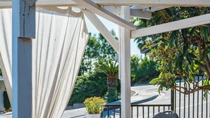 An outdoor patio with a white pergola, a table with chairs, and a potted plant. - Modern 5BR Villa w AC Fast Wifi Near Crypto (Monterey Park)