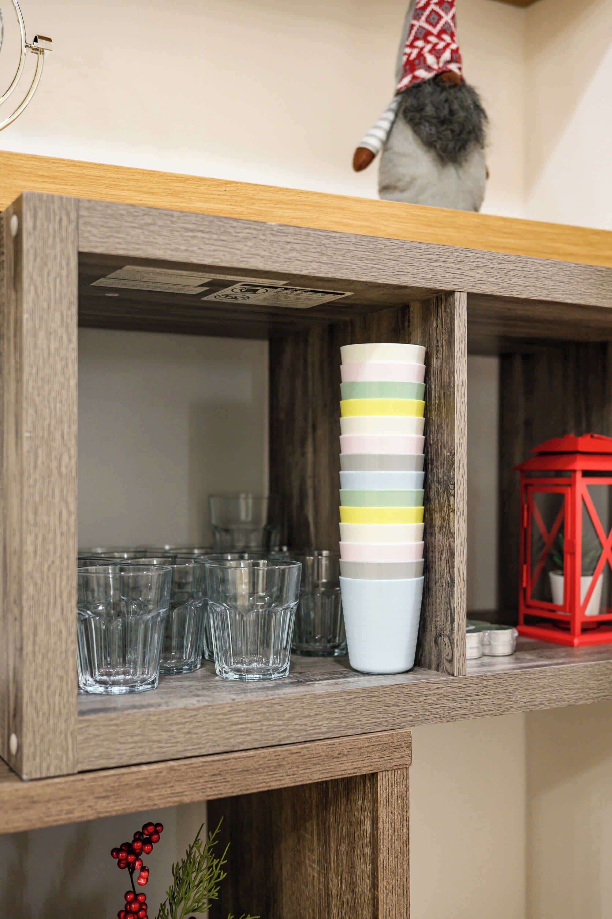 Une étagère en bois sur laquelle sont disposés plusieurs verres transparents, une pile de tasses colorées et une lanterne rouge.