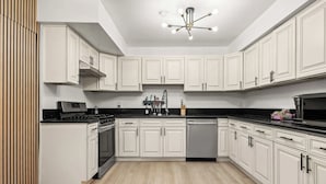A modern kitchen with white cabinetry, a black countertop, and a stainless steel range hood. - Modern 5BR Villa w AC Fast Wifi Near Crypto (Monterey Park)