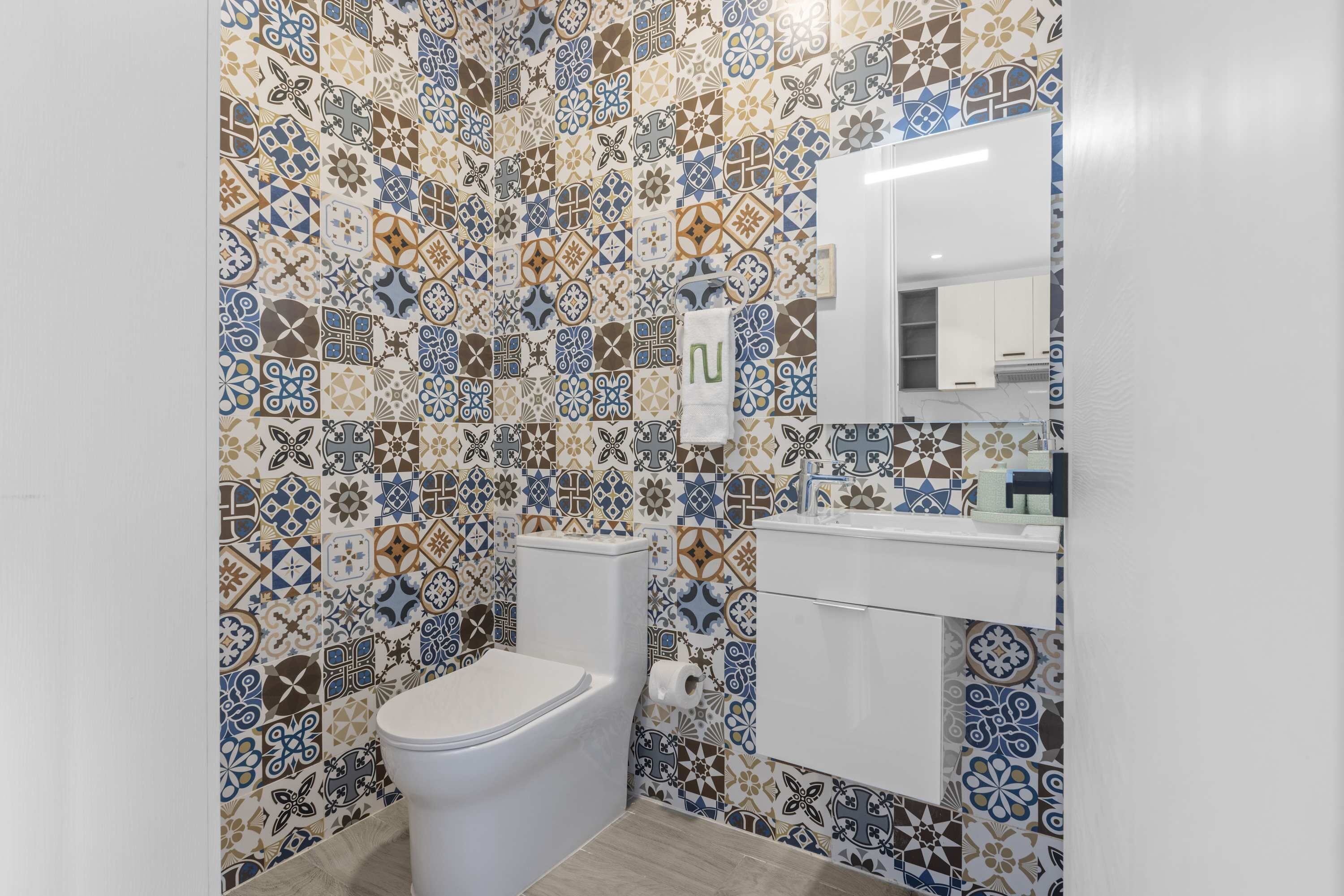 A bathroom with a patterned tile wall, a toilet, a sink, and a mirror.