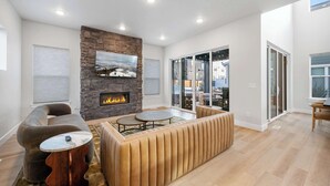 A modern living room with a stone fireplace, a large window, and a cozy seating area. - Ski Chalet Chic Retreat With Hot Tub (Park City)