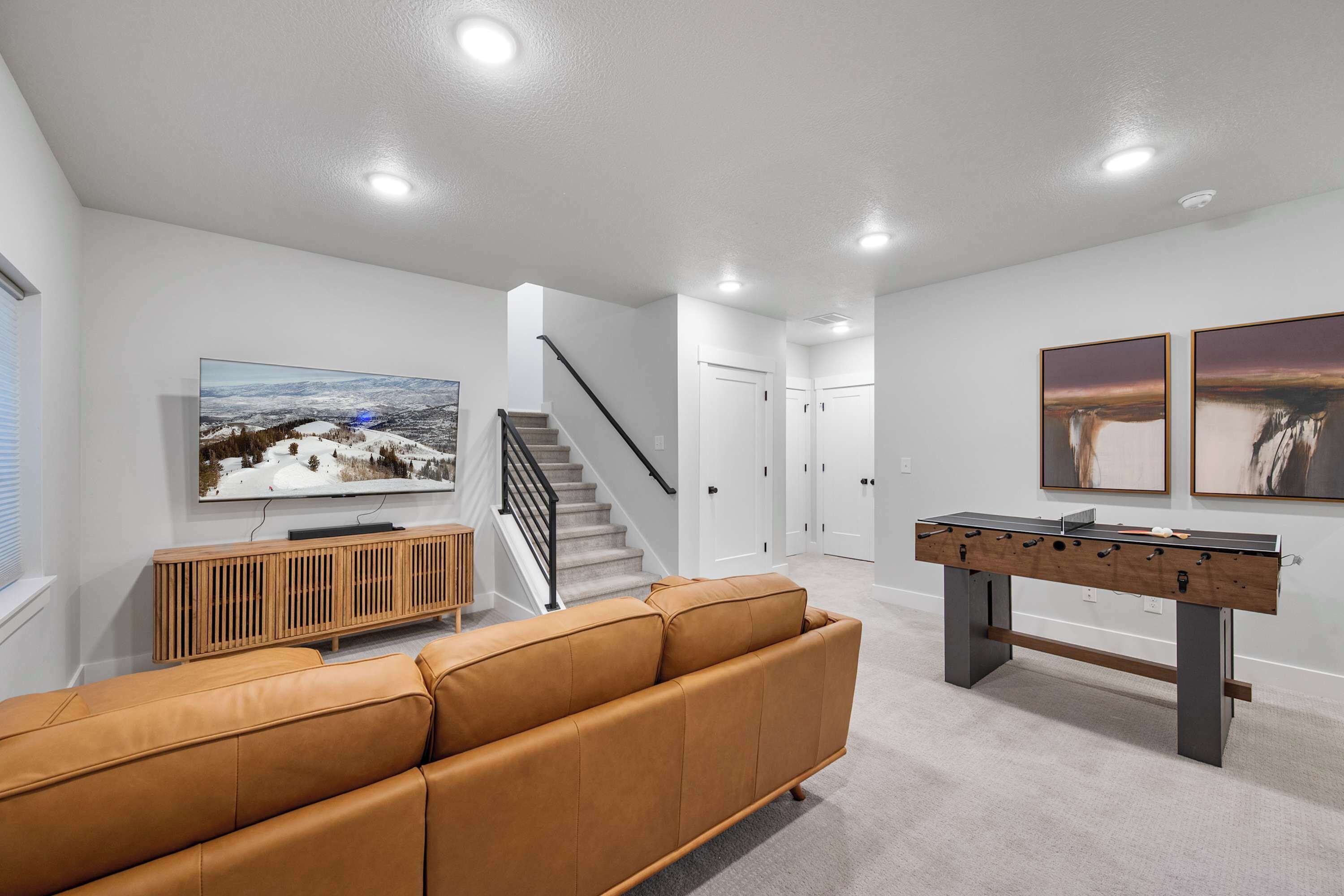 A modern living room with a sofa, a foosball table, a TV, and a staircase.