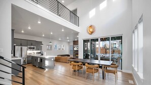 A spacious kitchen with modern appliances, a dining area with wooden chairs, and a view of the outdoors through large windows. - Ski Chalet Chic Retreat With Hot Tub (Park City)