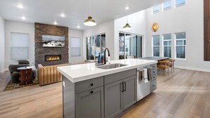 A spacious kitchen with a large island, a stone fireplace, and a view of the outdoors. - Ski Chalet Chic Retreat With Hot Tub (Park City)