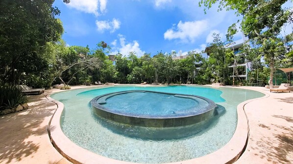 A swimming pool with a hot tub in the center, surrounded by lounge chairs and trees. - Anana Yaaxlum 106 S Familly Condo Oasis Pool (Tulum)