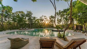 Un espace piscine aménagé avec des chaises longues et une piscine circulaire, le tout entouré d’arbres et de verdure.