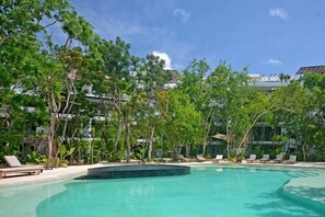 A pool area with lounge chairs and trees, surrounded by buildings. - Anana Yaaxlum 106 S Familly Condo Oasis Pool (Tulum)