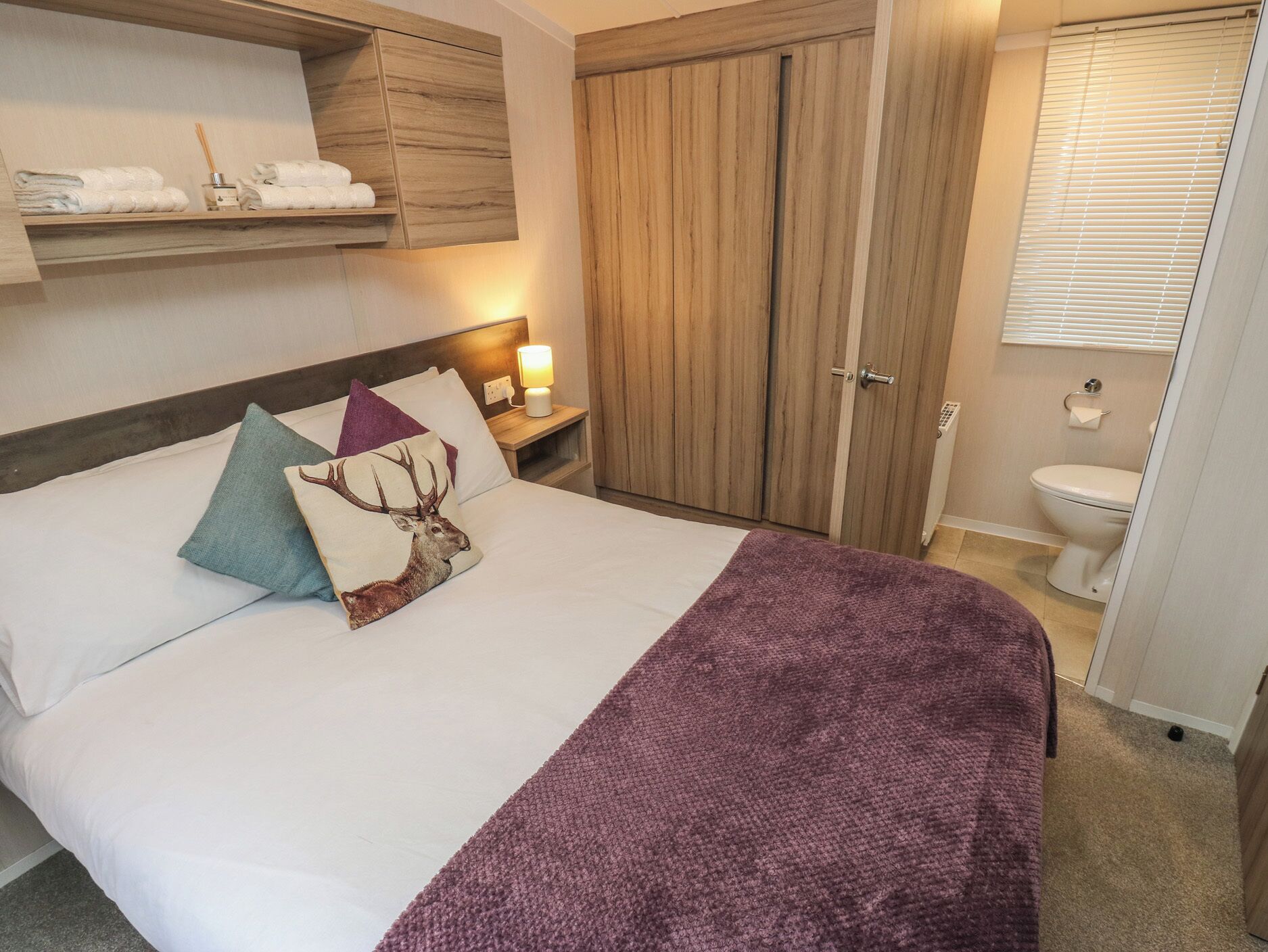 A hotel room with a bed, a nightstand, a wooden wardrobe, and a bathroom with a toilet and window.