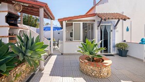 A patio area with a stone planter, a grill, and a dining table. - Holiday Home 'Shellls Apartment' with Shared Terrace, Wi-Fi and Air Conditioning (Carvoeiro)