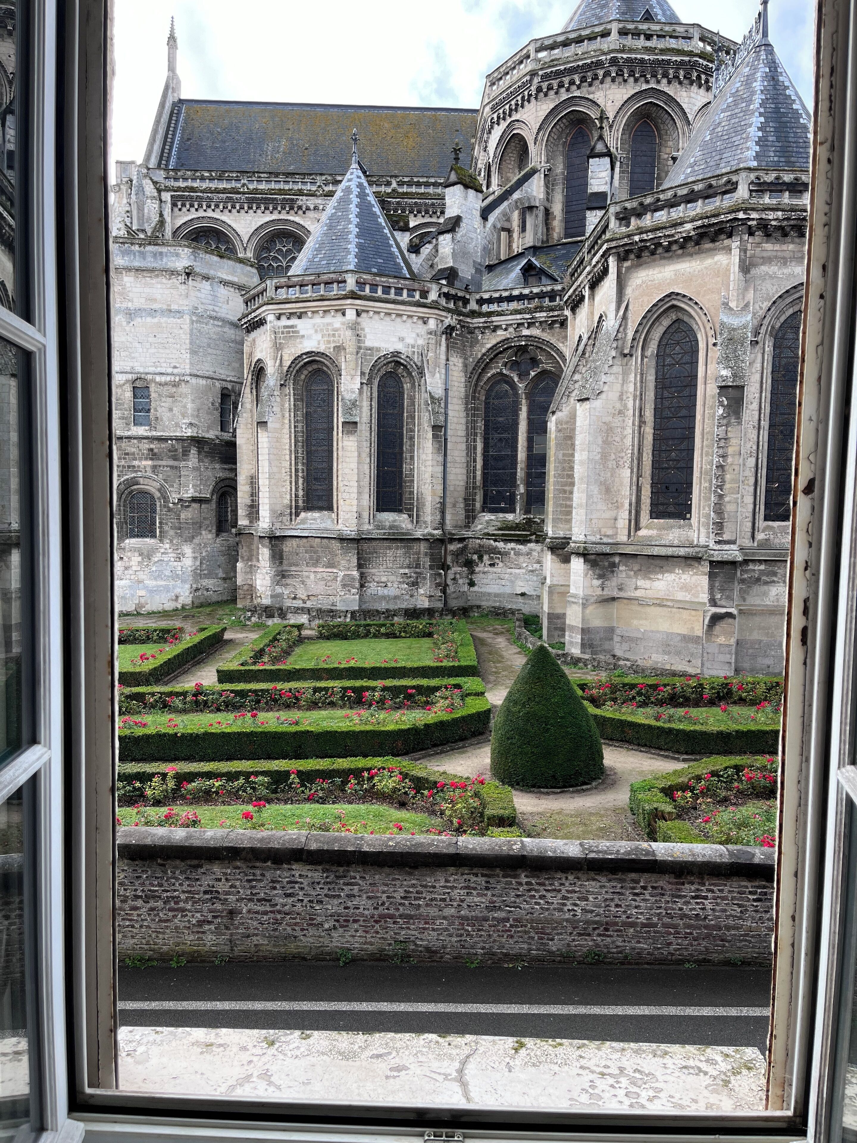 A historic building with a courtyard featuring geometric garden beds and a central tree.