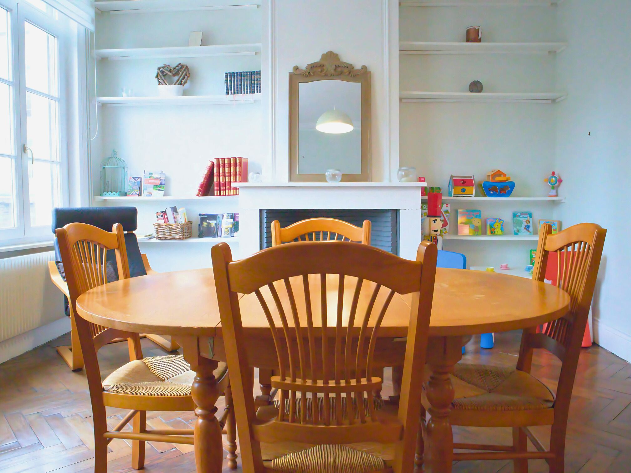 Zona pranzo con tavolo rotondo in legno e quattro sedie, circondata da scaffali bianchi con libri e oggetti decorativi.