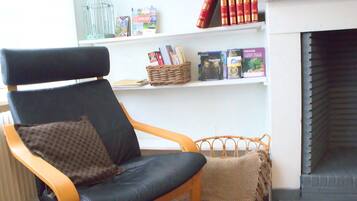 Una habitación con una silla de madera, una chimenea y una estantería con libros y objetos decorativos.