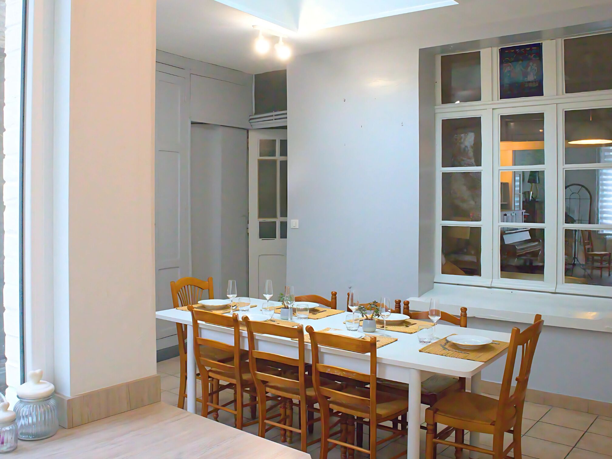 Zona pranzo con tavolo bianco apparecchiato per sei persone, circondato da sedie in legno.
