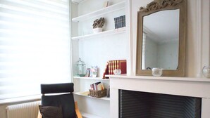 Ein Wohnzimmer mit Kamin, einem schwarzen Sessel, einem Bücherregal und einem Spiegel.