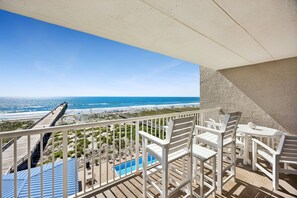 Ein Balkon mit weißen Stühlen und einem Tisch mit Blick auf Strand und Pool.