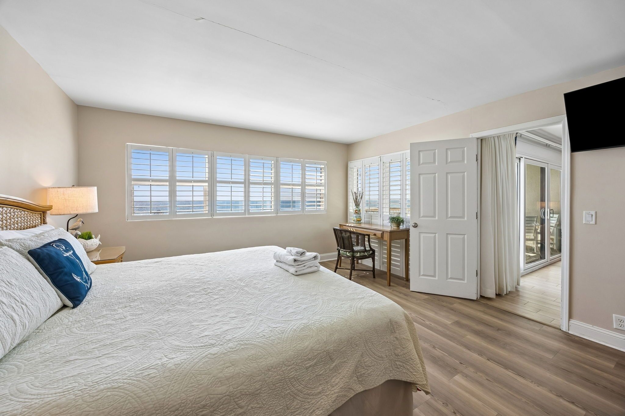 A bedroom with a large bed, a desk, and a view through a door.