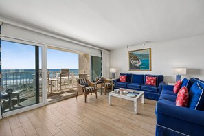 Uma sala espaçosa com varanda, um conjunto de sofás azuis e um quadro na parede.