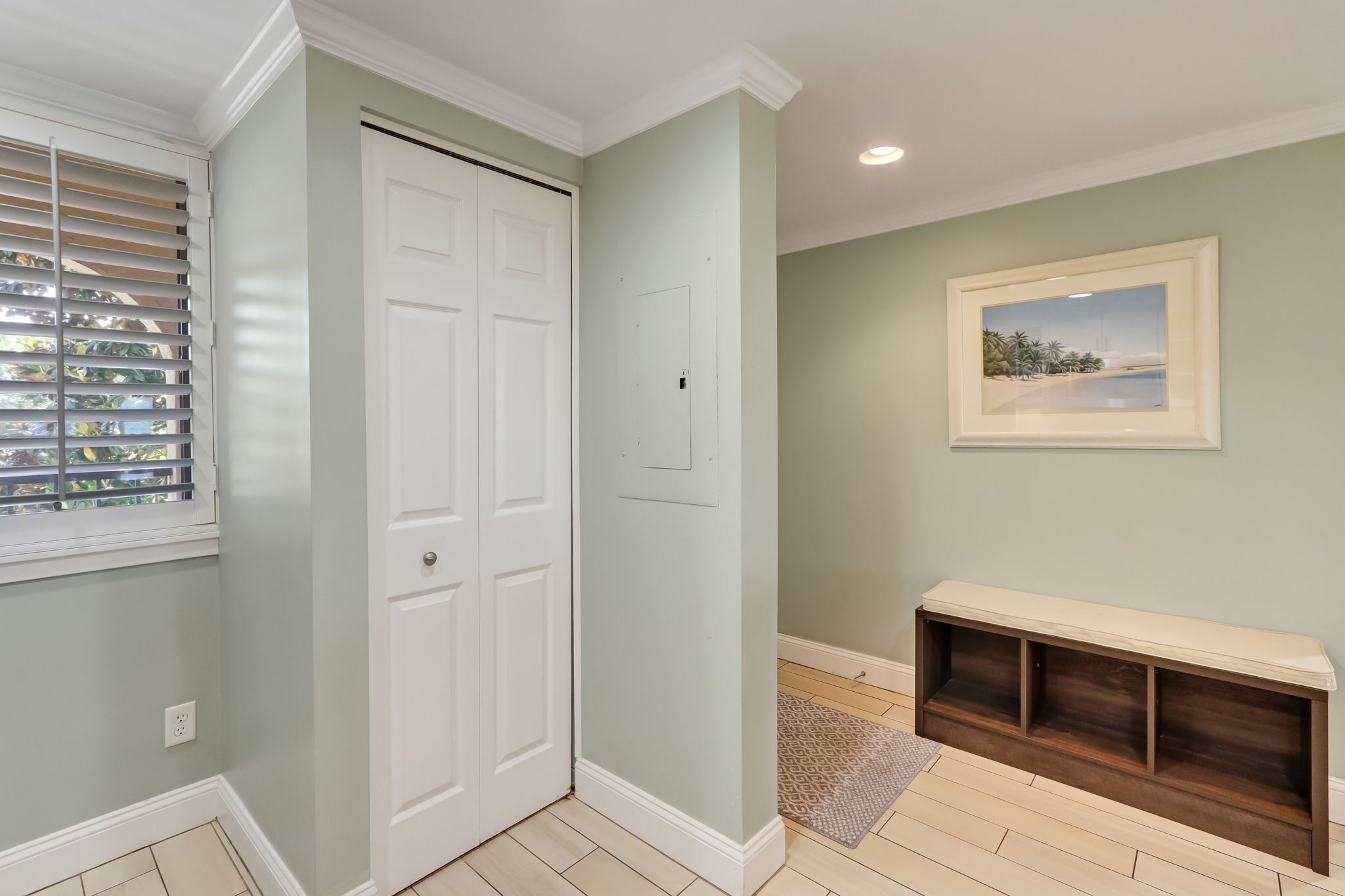 A hallway with a white door, a bench, and a framed picture on the wall.