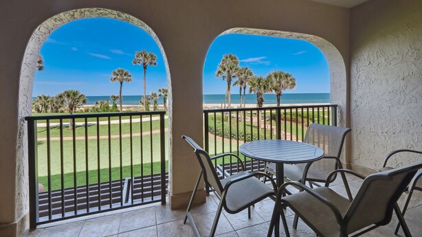 A balcony with a view of a golf course and palm trees, a round table, and four chairs. - Cozy Pet Friendly Condo by The Beach Omni Sea Dunes - 1616 (Fernandina Beach)