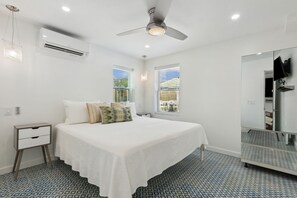 Quarto de hotel moderno com cama, mesa de cabeceira, aparelho de ar condicionado, ventilador de teto e espelho grande.
