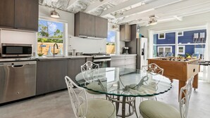 Una cocina moderna con electrodomésticos de acero inoxidable, una mesa de comedor de vidrio y una mesa de futbolín.
