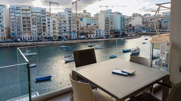 Ein Balkon mit Tisch und Stühlen mit Blick auf einen Yachthafen und Gebäude.