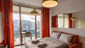 Ein Hotelzimmer mit Bett, Sofa, Schreibtisch und Blick auf eine Stadtlandschaft durch große Fenster.