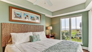 Una camera da letto con un letto grande, una testiera in tessuto, vista sull'esterno e opere d'arte incorniciate al muro.