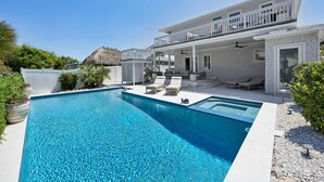 Une maison à deux étages avec une piscine, un espace extérieur aménagé et une structure dotée d’un toit de chaume.